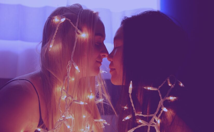 two woman facing each other with string lights